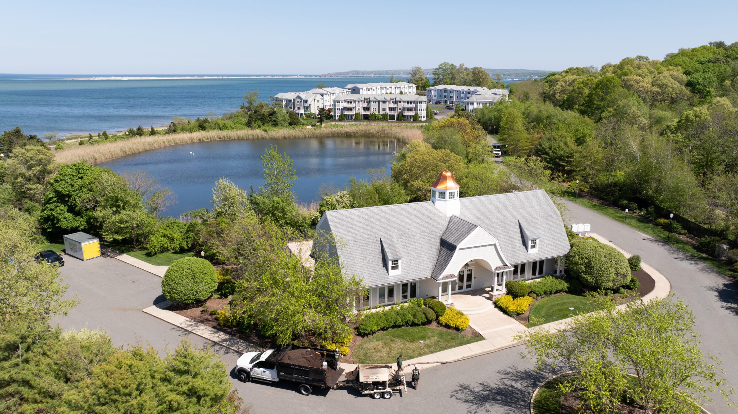 A picturesque lakeside building using coastal landscaping ideas with a copper dome in a verdant landscape, near a residential area and expansive body of water.