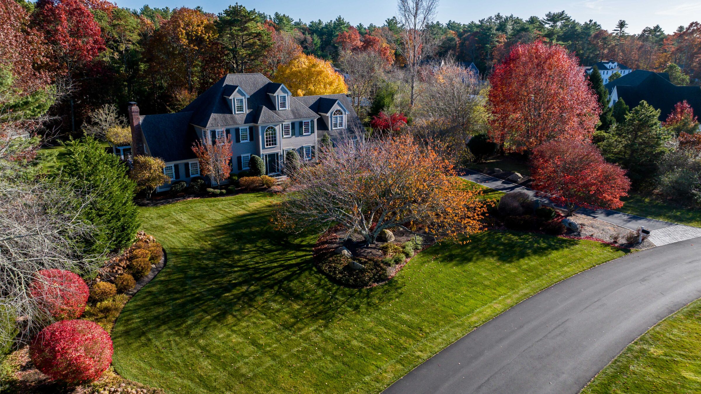 Elegant house amidst vibrant autumn foliage, surrounded by trees, lawn, and a curved driveway. Peaceful, picturesque setting with no visible persons.
