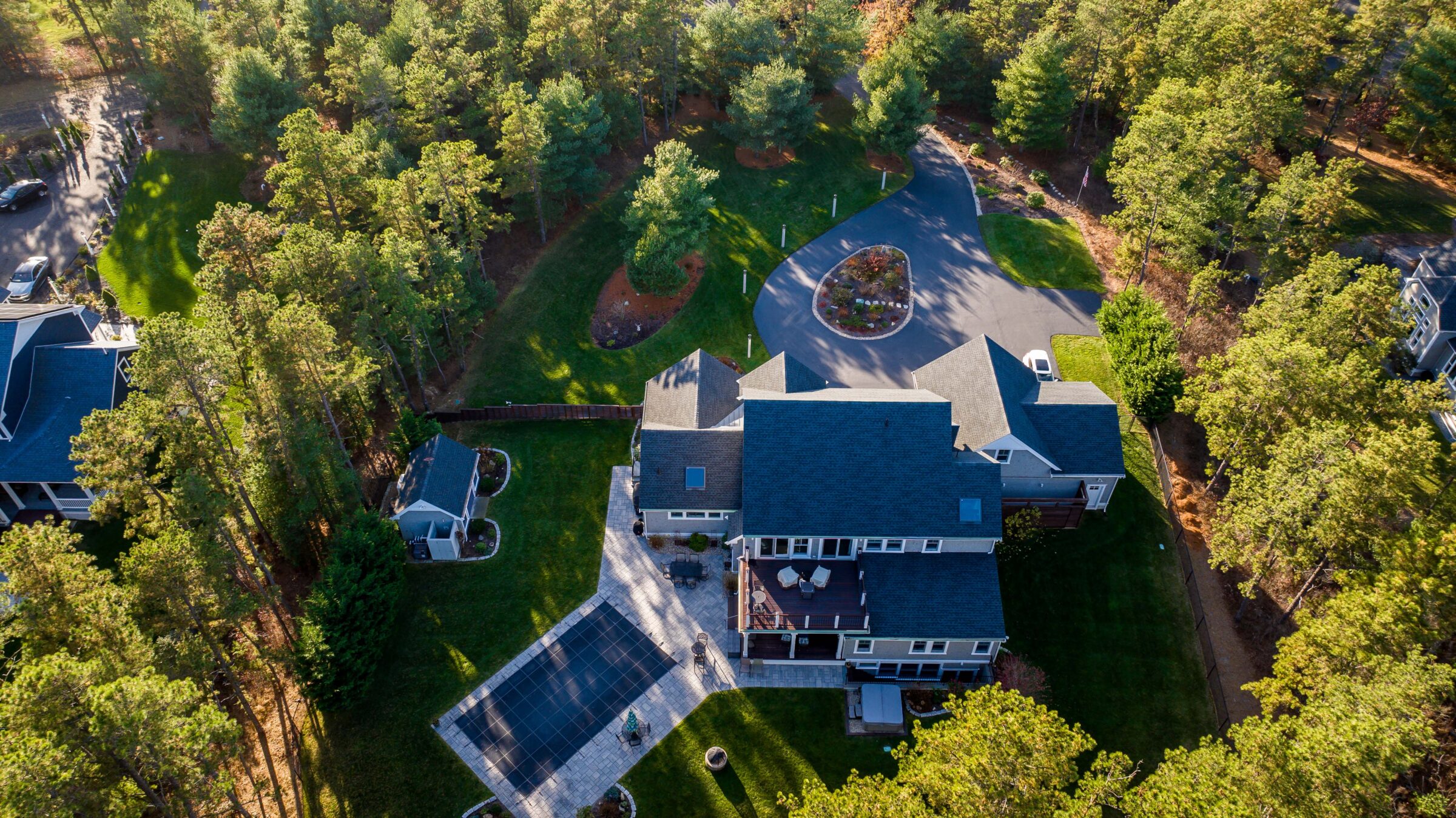 Aerial view of a large house surrounded by trees, with a driveway and a swimming pool. Peaceful, suburban setting.
