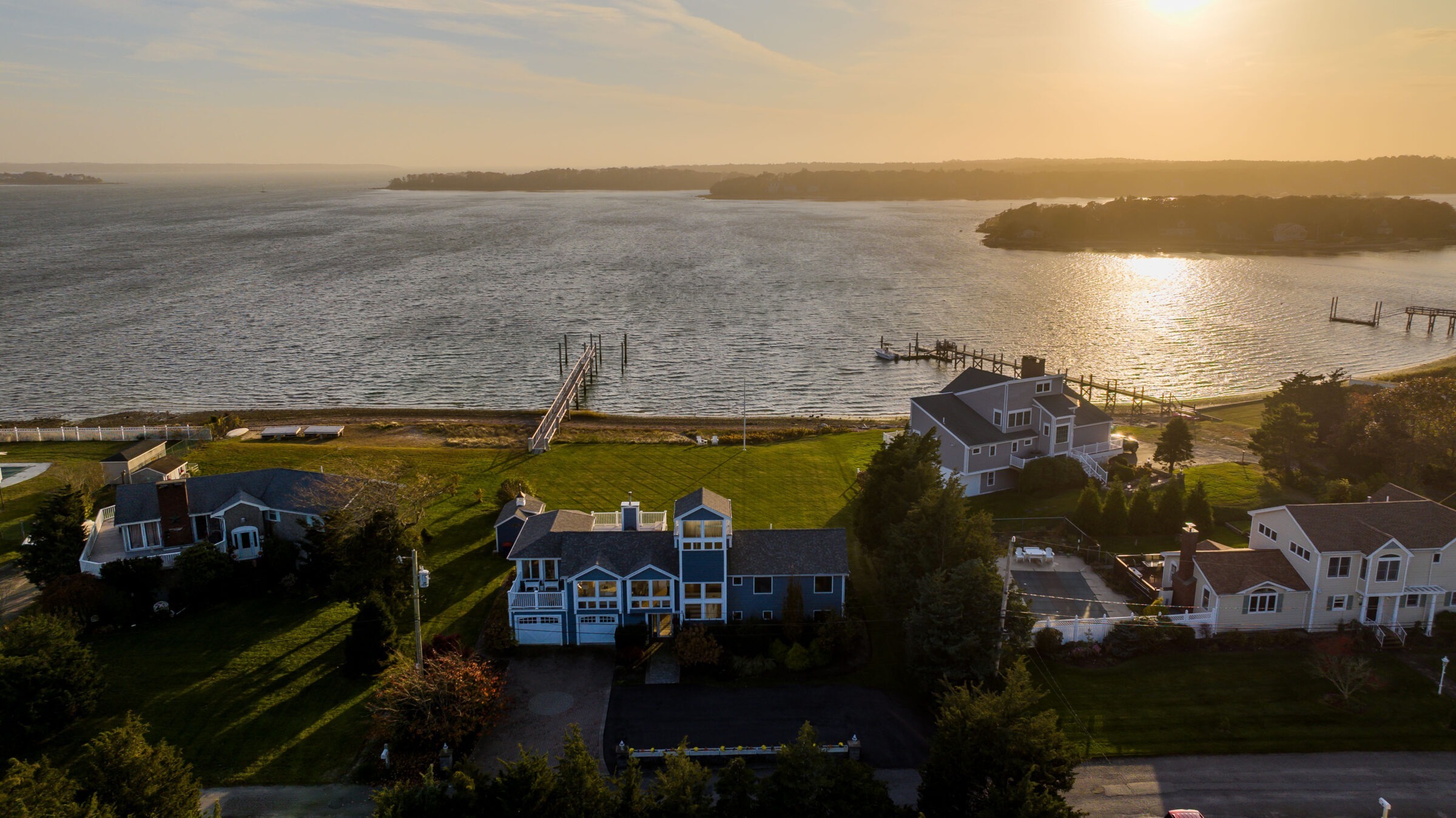 Aerial view of waterfront homes at sunset, featuring docks leading to the serene body of water and a warm, glowing horizon.