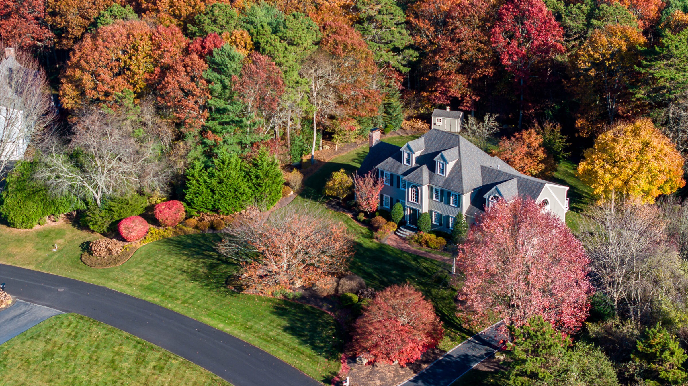 Aerial view of a large house surrounded by vibrant autumn trees and a winding driveway on a well-maintained lawn.