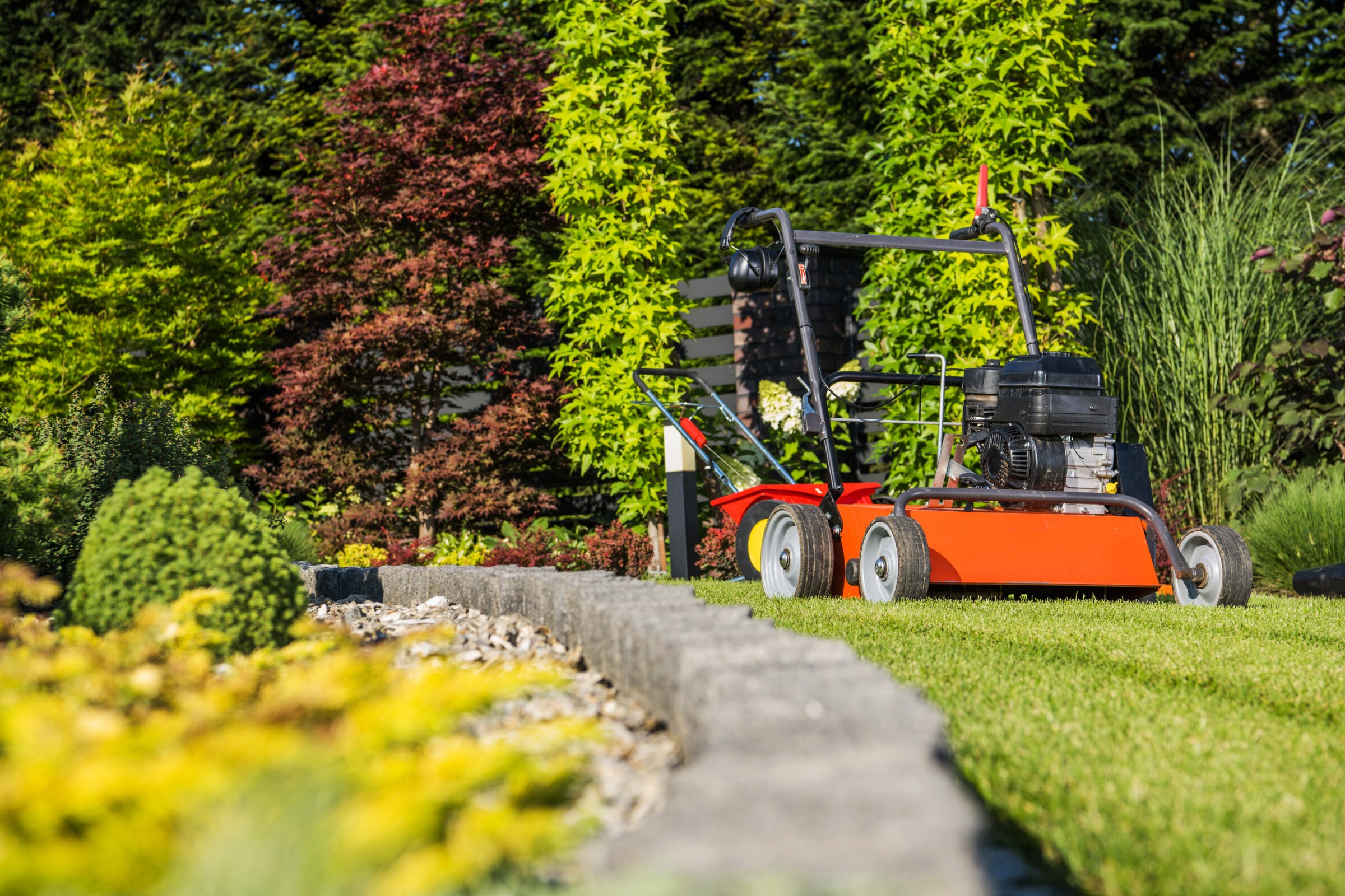 An orange lawnmower in front of a line of bushes and a line of stones outlining a garden from ground level.