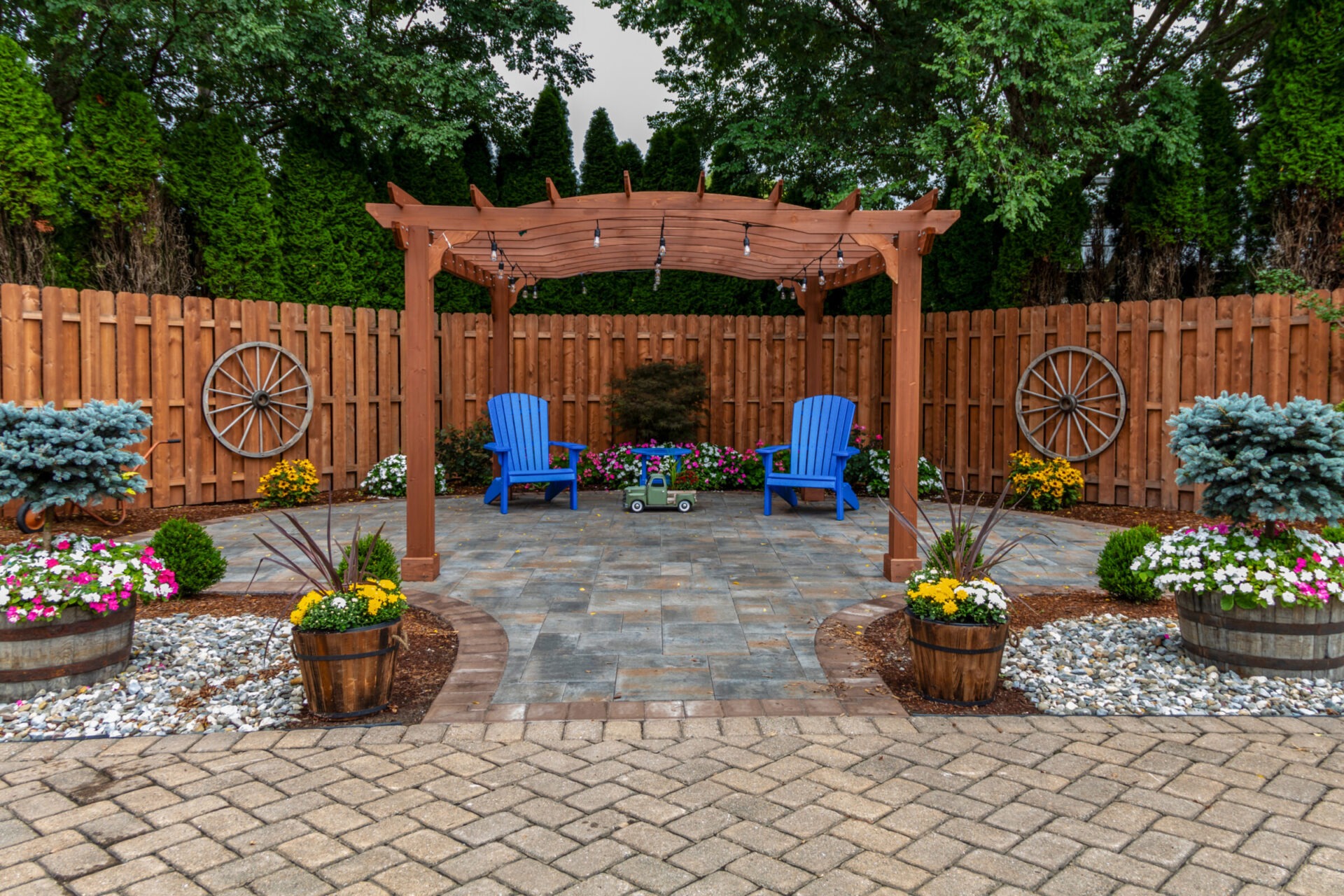 Cozy backyard with wooden pergola, blue chairs, vibrant flowers, and a decorative fence, creating a tranquil, inviting garden space for relaxation.