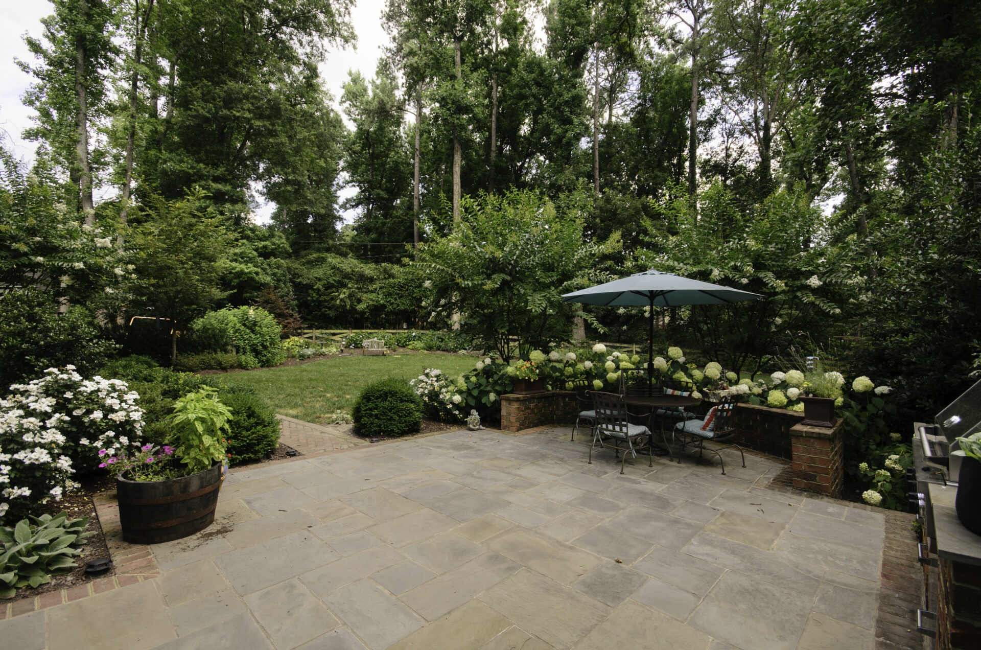 A beautiful backyard patio featuring stone flooring and seating surrounded by lush greenery, perfect for outdoor relaxation and enjoying nature in a serene atmosphere.