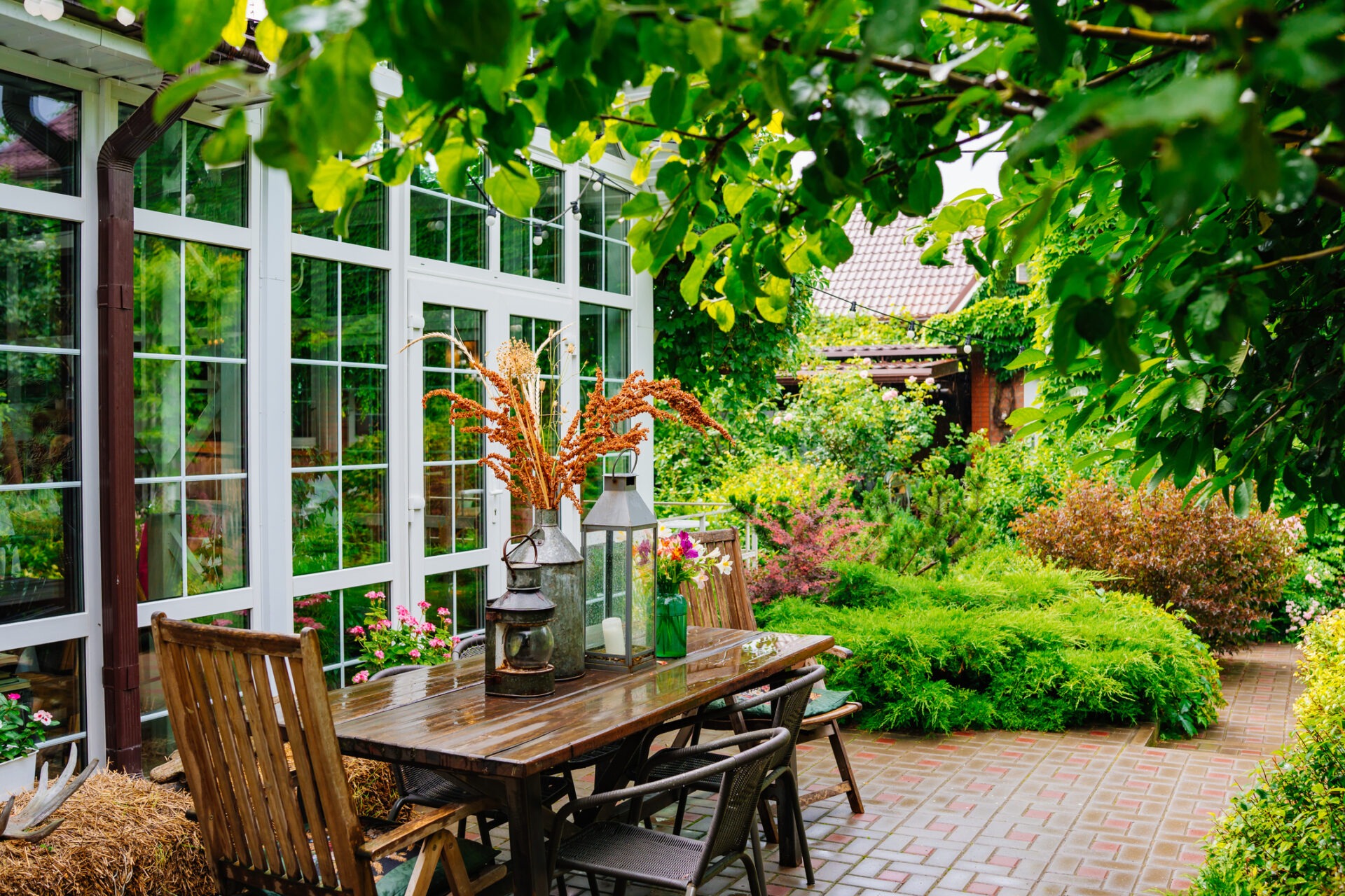 wooden table with lanterns and dried flowers. The yard in the house is with panoramic glazing. decor for a garden or park. Cozy summer courtyard.