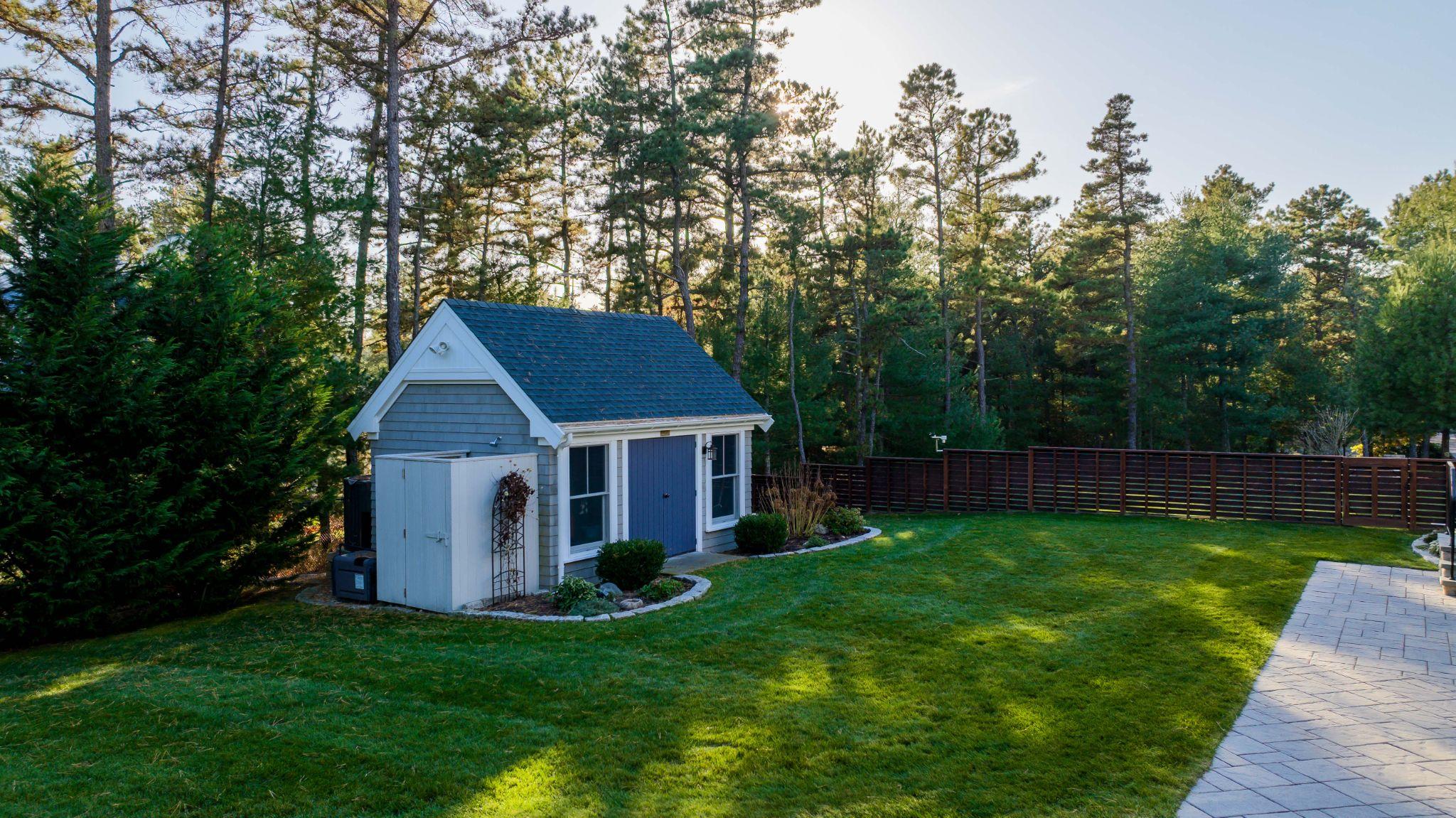 Backyard lawn with shed, patio, and trees in a wooded Plymouth County property